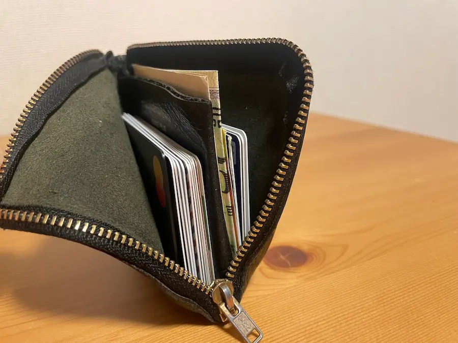 コム・デ・ギャルソンのL字ファスナーの財布が開き、中にクレジットカードやお札が入っている様子。