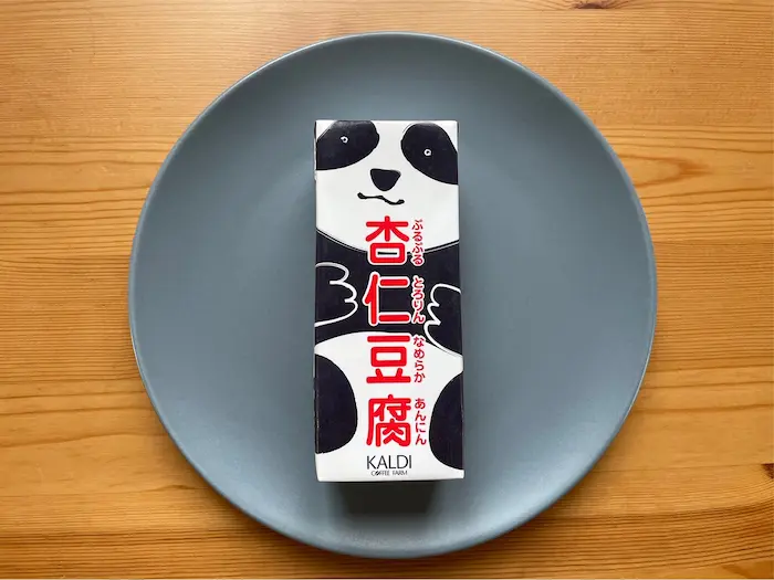 木の机の上に青いお皿に乗ったカルディで売っているパンダの柄の杏仁豆腐が載っている写真