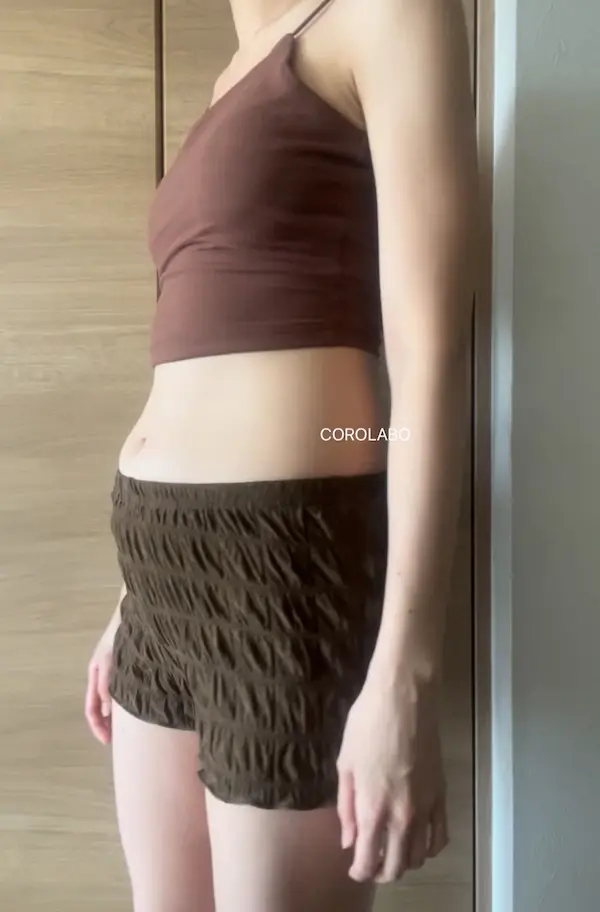 木の扉の前にショートパンツとクロップド丈トップスを着た人のお腹周りが映った写真
