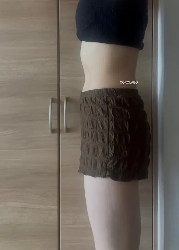 木の扉の前にショートパンツとクロップド丈トップスを着た人のお腹周りが映った写真
