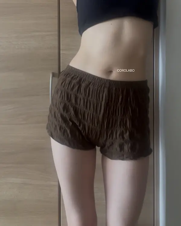 木の扉の前にショートパンツとクロップド丈トップスを着た人のお腹周りが映った写真