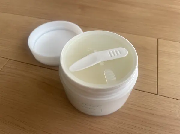 白いジャータイプの入れ物の蓋が開けられ、スパチュラが内蓋に載っている様子